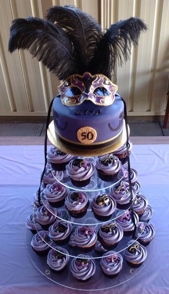 a tiered cake decorated with cupcakes and an ostrich mask