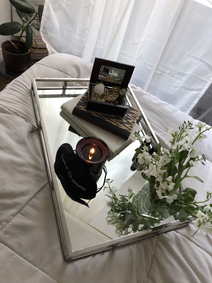 a tray with flowers and a candle on it sitting on top of a white bed