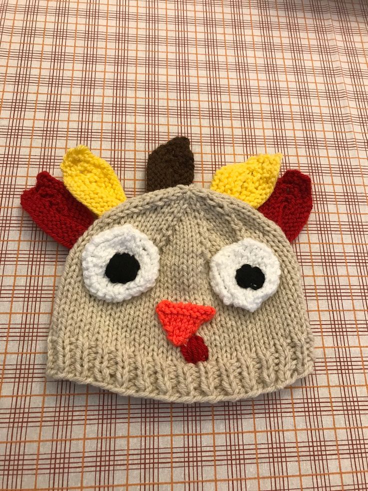 a knitted hat with a chicken face on top of a plaid cloth tablecloth