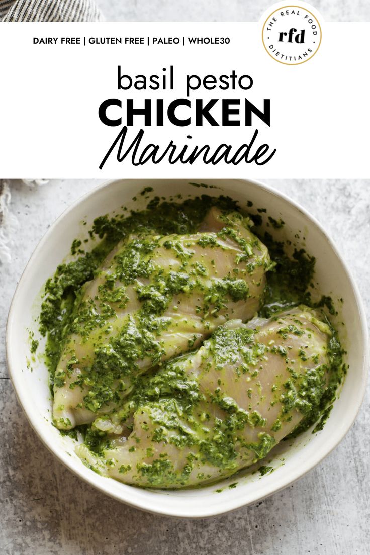 a white bowl filled with chicken covered in pesto and parsley on top of a table