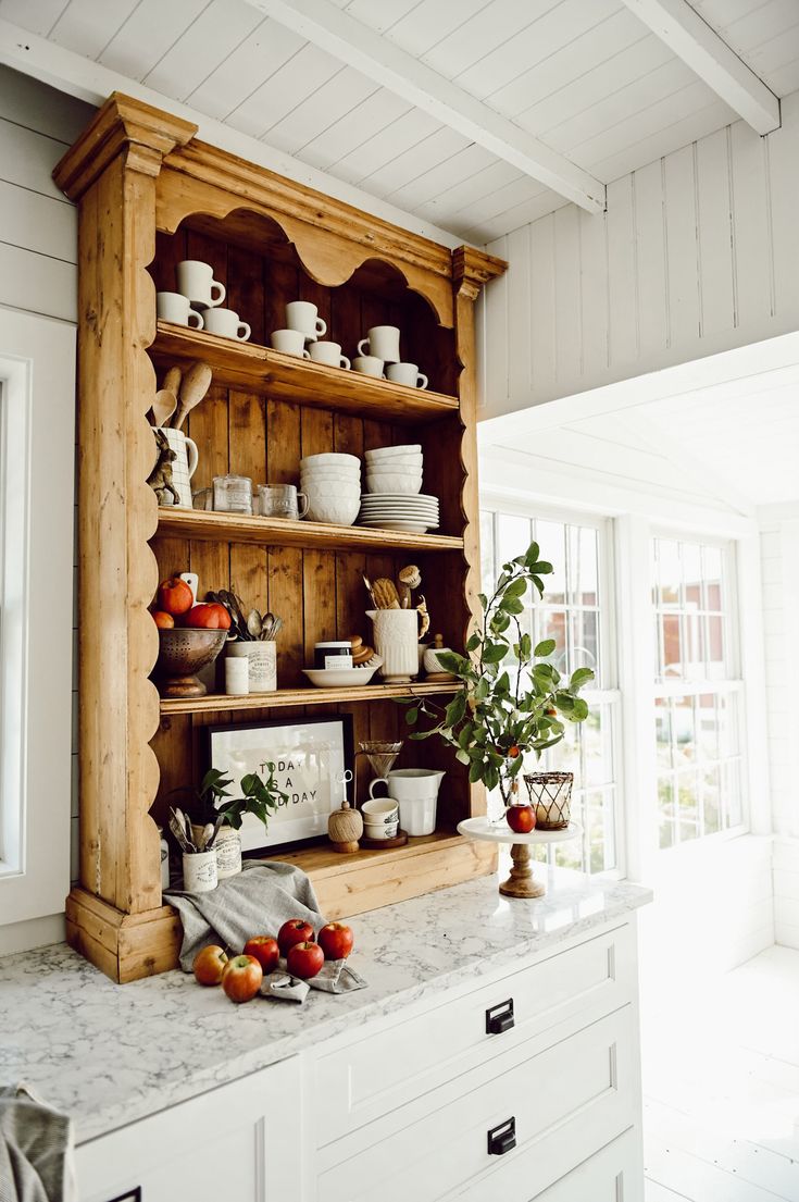 a kitchen with white cabinets and marble counter tops, an open shelf filled with dishes