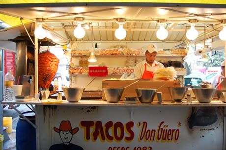 a man standing behind a food cart selling tacos