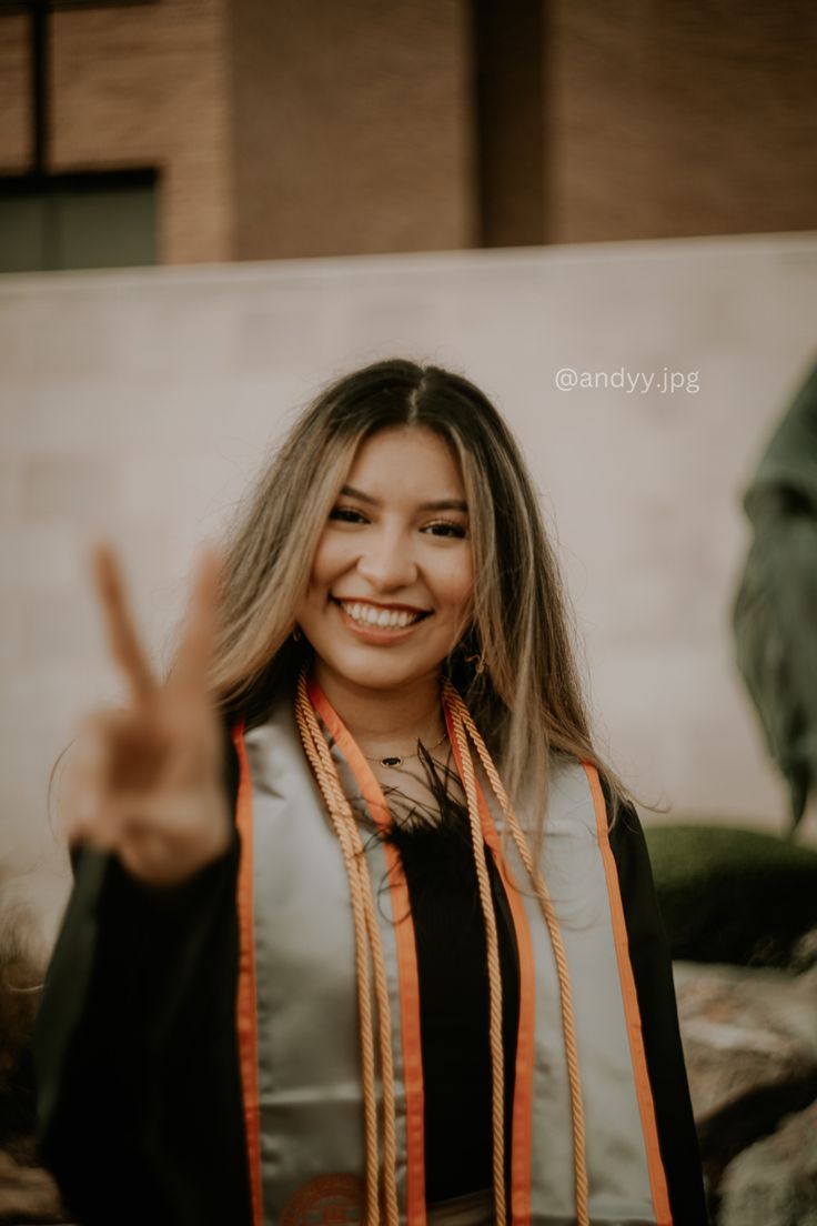 a woman with long blonde hair wearing an orange and black scarf giving the peace sign