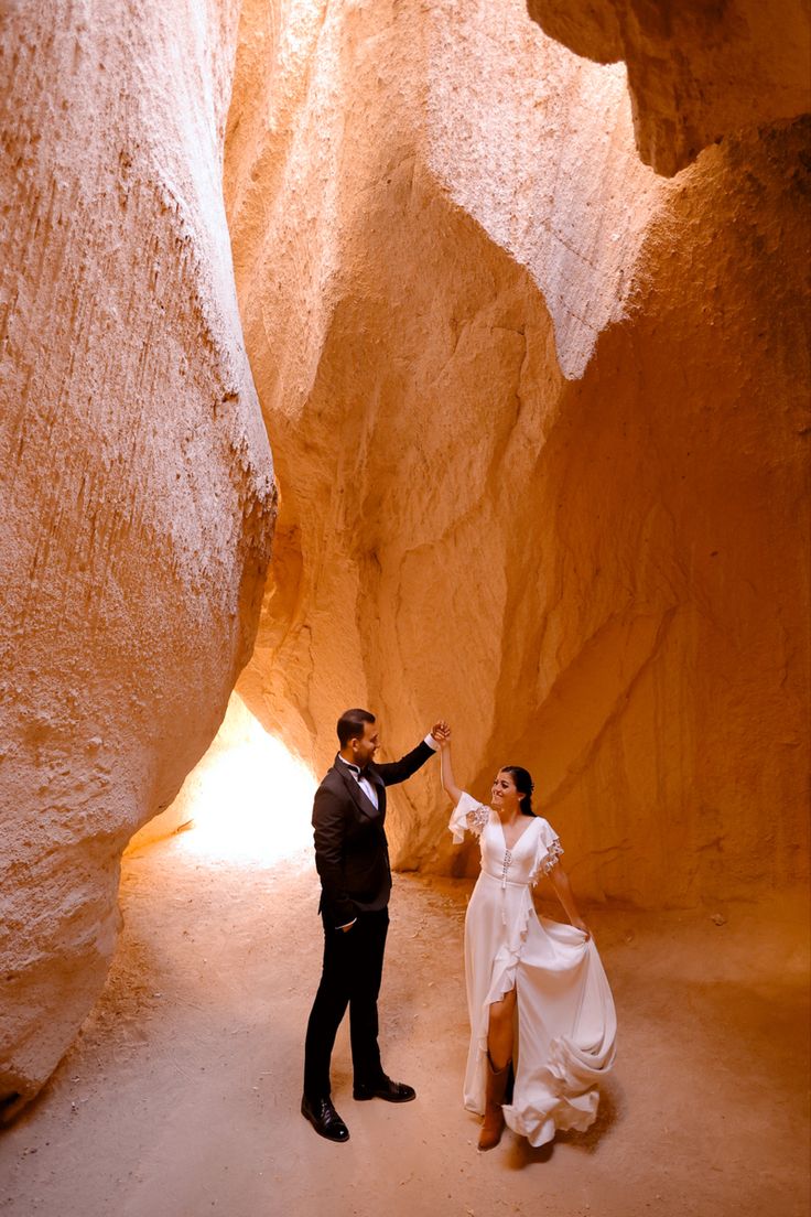 a man and woman are standing in the middle of a narrow slot between two large rocks