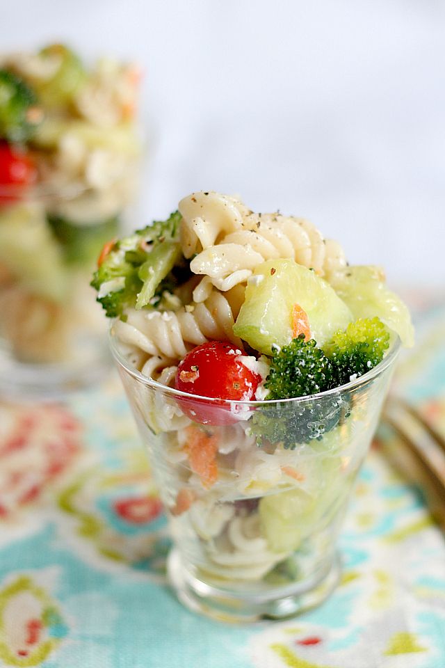 two small bowls filled with pasta salad on top of a floral table cloth next to utensils