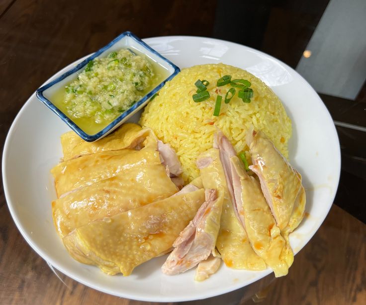 a white plate topped with meat and rice next to a bowl of green dipping sauce