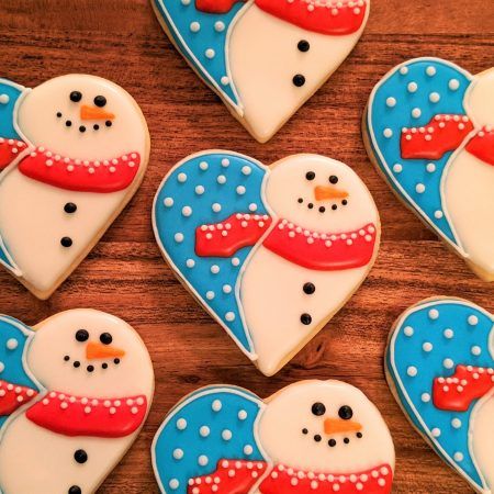 decorated cookies in the shape of hearts with snowmen on them, arranged on a wooden table