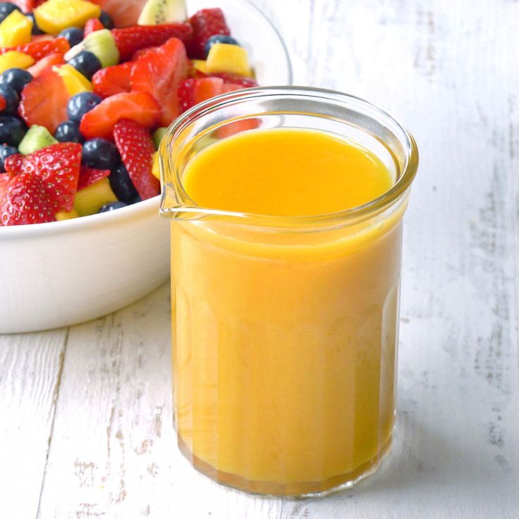 a glass jar filled with orange juice next to a bowl of fruit