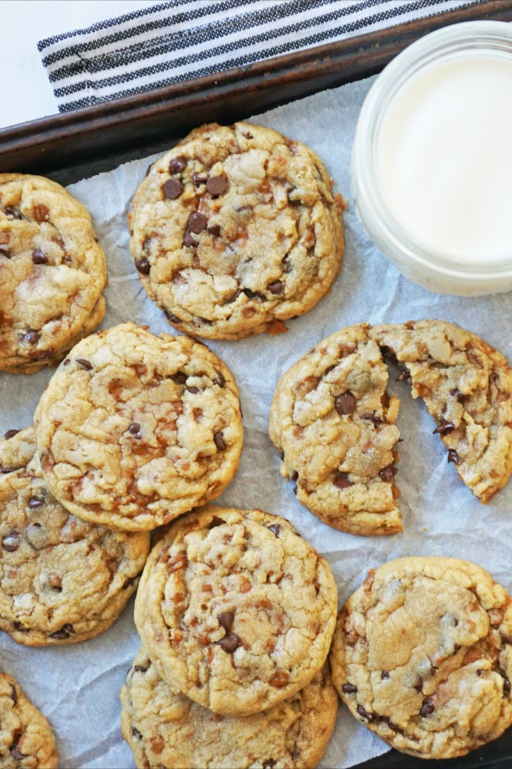 chocolate chip cookies and a glass of milk on a tray with parchment paper next to it