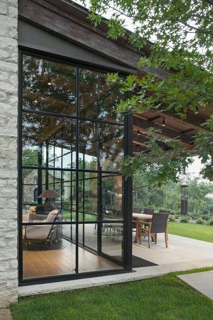 an open patio with glass walls and sliding doors on the side of it, surrounded by grass