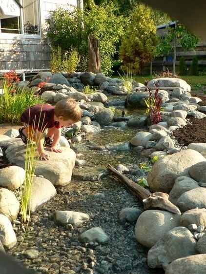 a young boy is playing with rocks in the water at his backyard garden, which has been designed to look like it's made out of stone