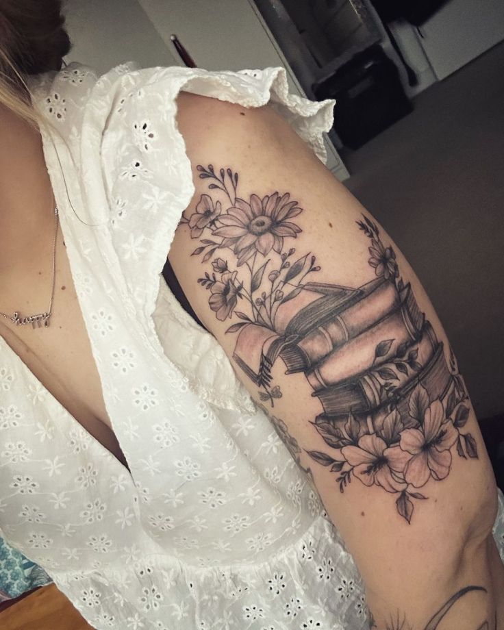 a woman with a tattoo on her arm is holding a stack of books and flowers