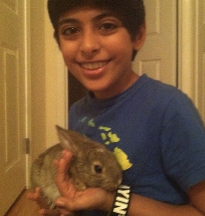 a boy is holding a small rabbit in his hands and smiling at the camera while wearing a blue t - shirt