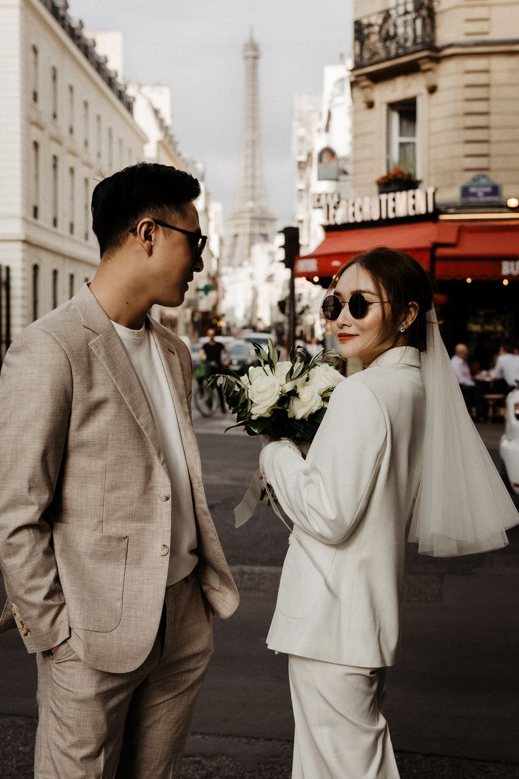 a man in a suit and tie standing next to a woman wearing sunglasses on the street