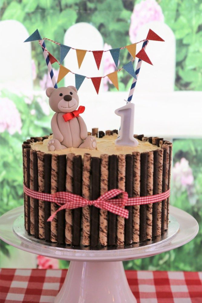 a teddy bear sitting on top of a cake with the number one frosted in it