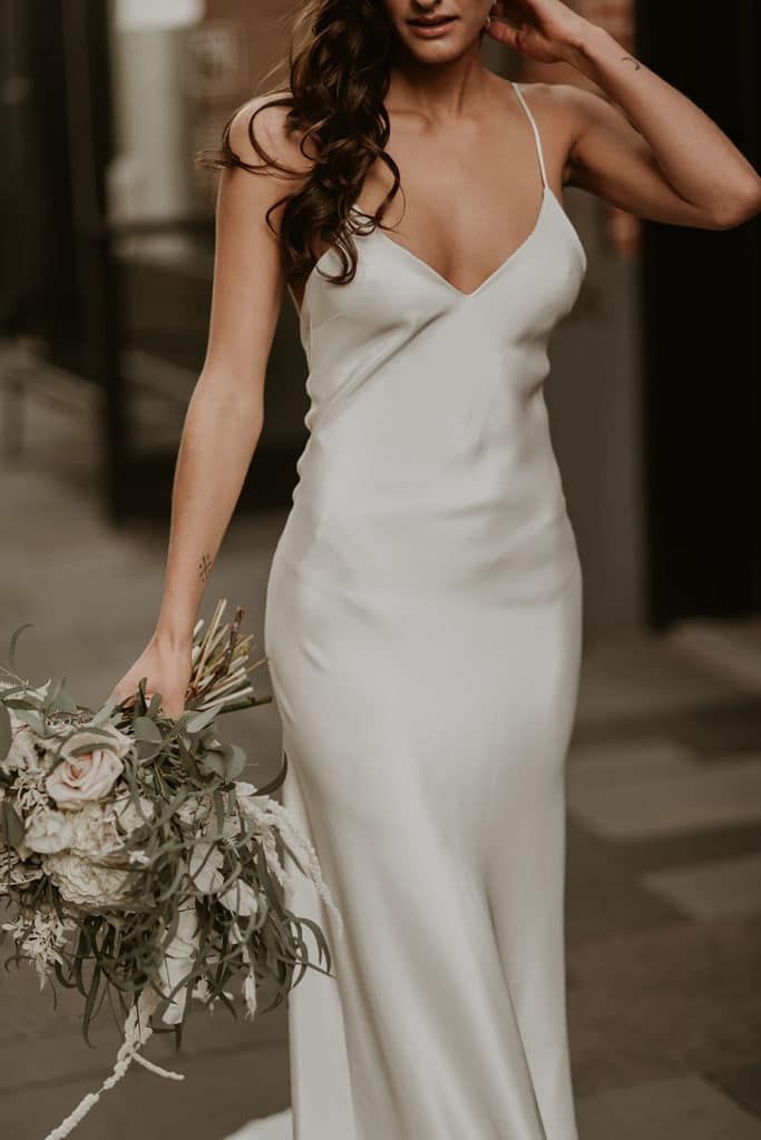 a woman in a white dress holding a bouquet and posing for the camera with her hand on her head