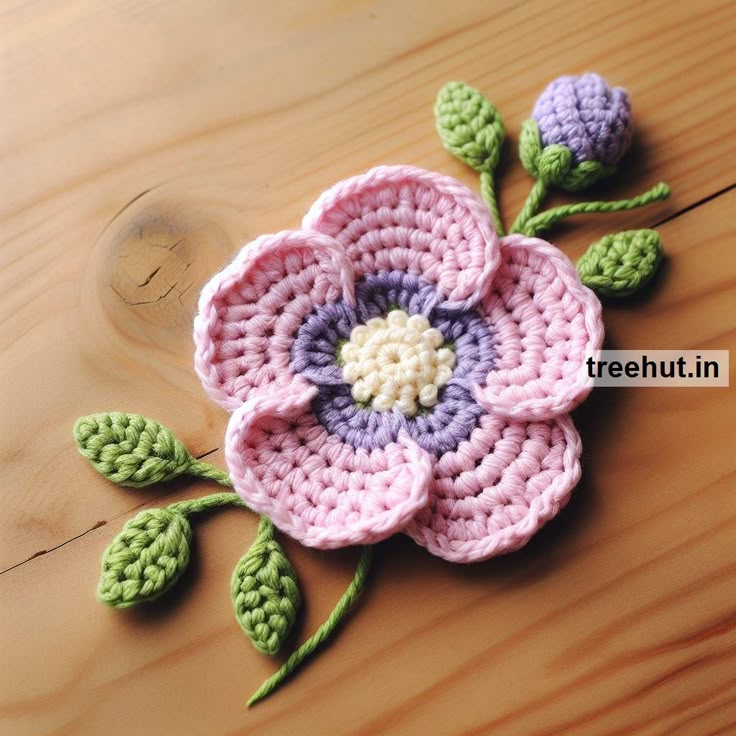 a crocheted flower is laying on a wooden surface with green leaves and purple petals