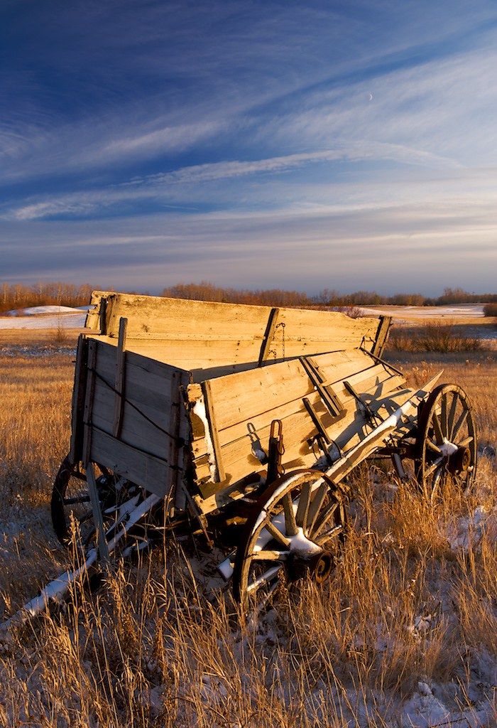 an old wooden wagon sitting in the middle of a field with snow on the ground