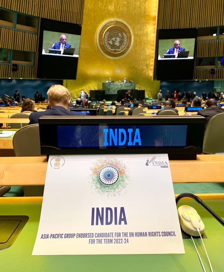 a table with a sign in front of it that says india and two men on the screen