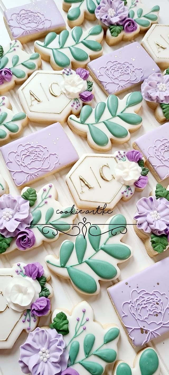 decorated cookies are arranged on a table with purple and green flowers in the center, along with white cookie cutters that spell out their names