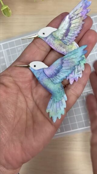 two small birds are being held in the palm of someone's hand on a table