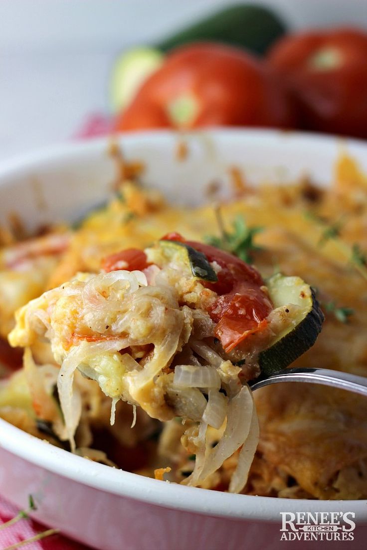 a spoon full of food that is in a bowl with tomatoes and other vegetables behind it