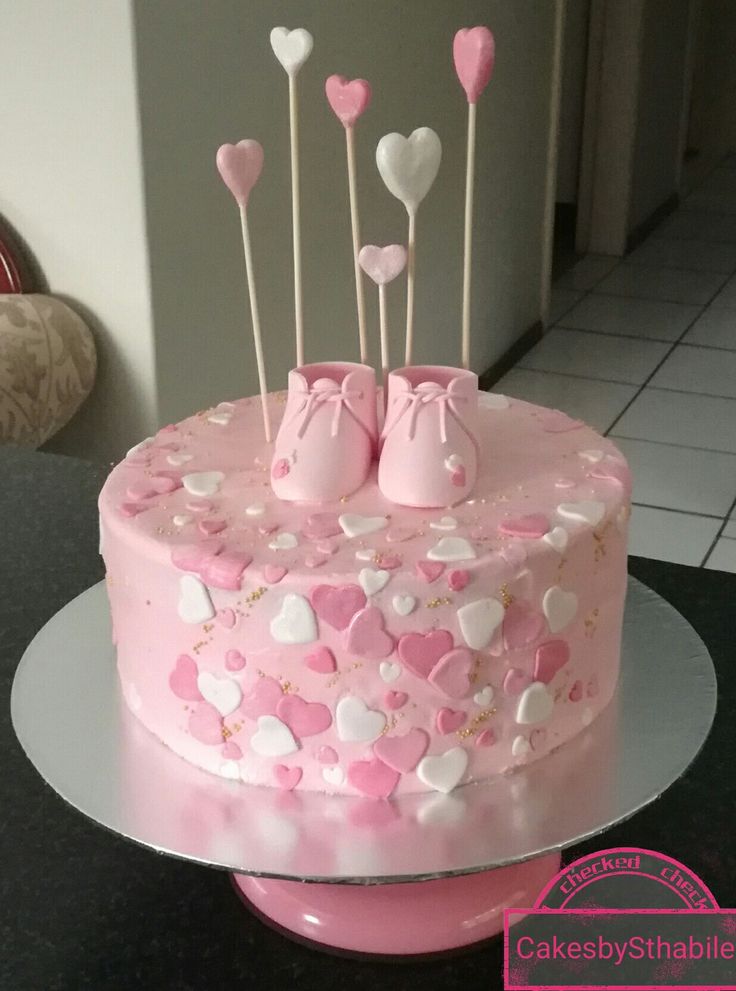 a pink cake decorated with hearts and baby shoes