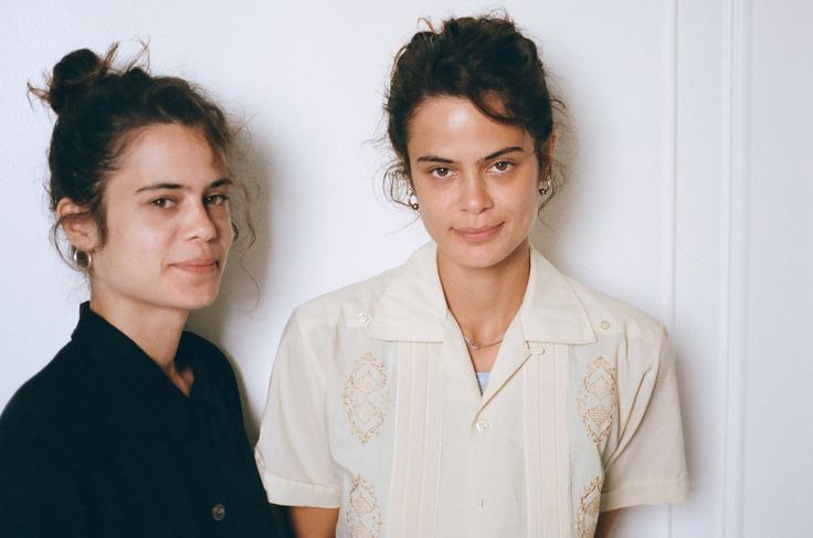 two young women standing next to each other in front of a white wall and door