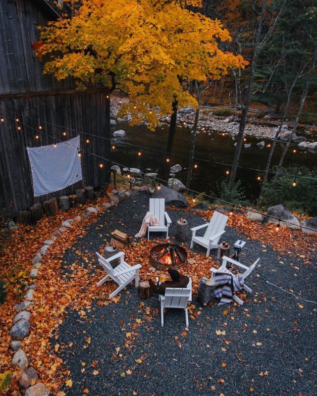 an outdoor fire pit surrounded by lawn chairs and string lights with fall leaves on the ground