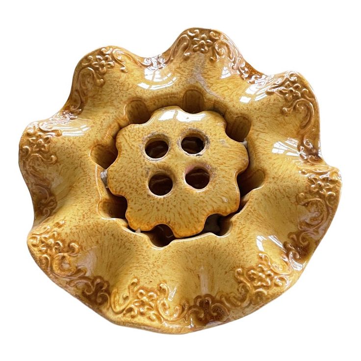 a yellow flower shaped bowl with two holes in the center and an intricate design on the bottom