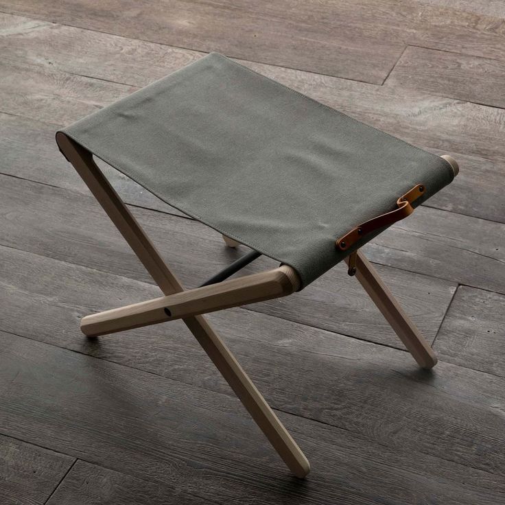 a small wooden stool with a leather seat on top of wood flooring in an empty room