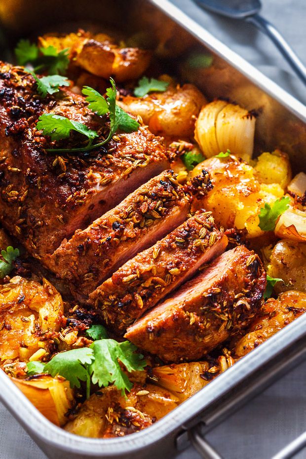 meat and potatoes in a roasting pan with garnishes on the side