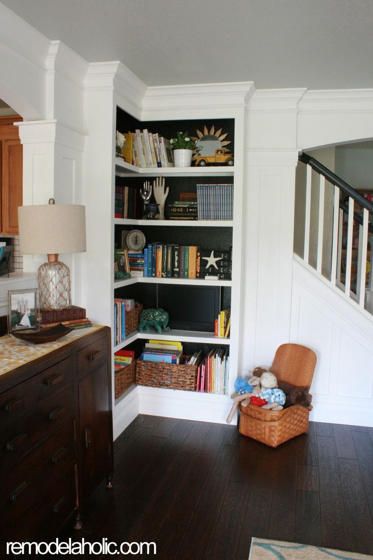 an open book shelf in the corner of a living room next to a stair case