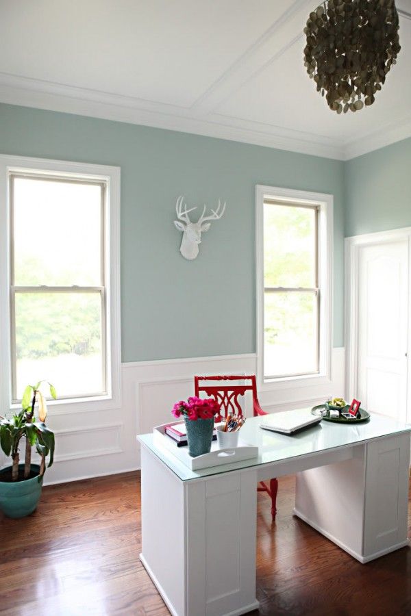 a room with two windows and a desk in the middle, along with plants on the other side