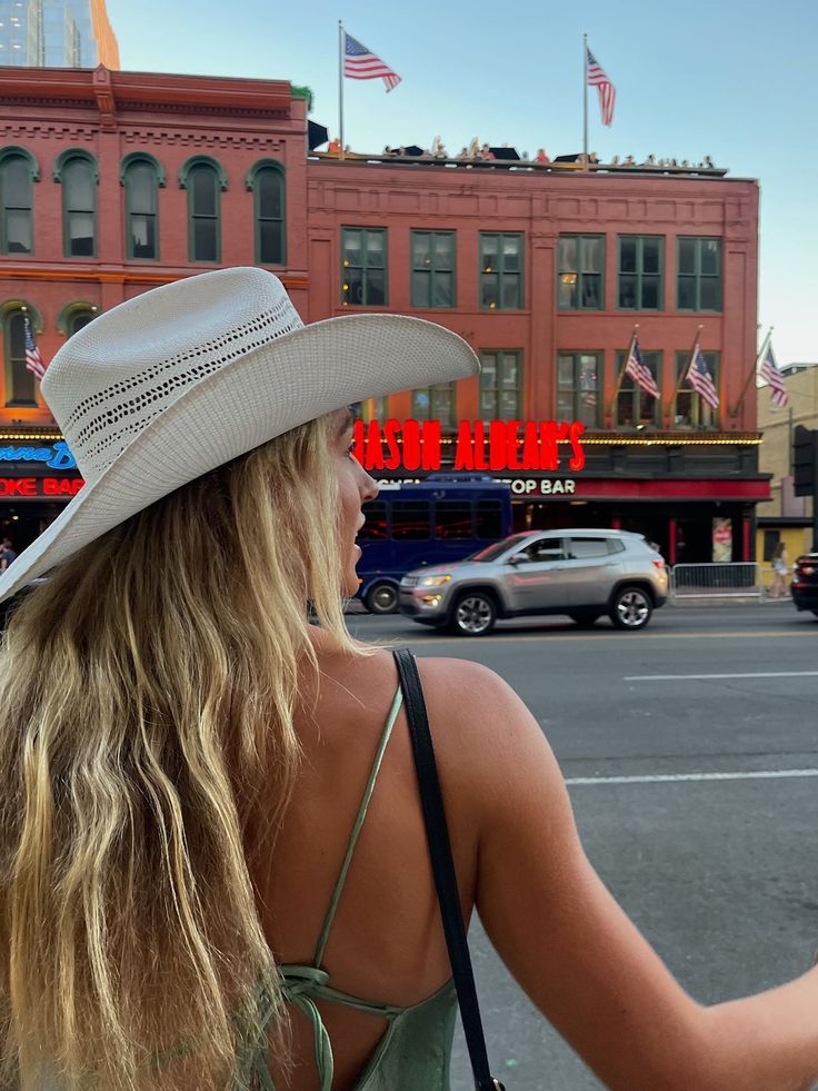 a woman in a white hat is looking at the street with cars and buildings behind her