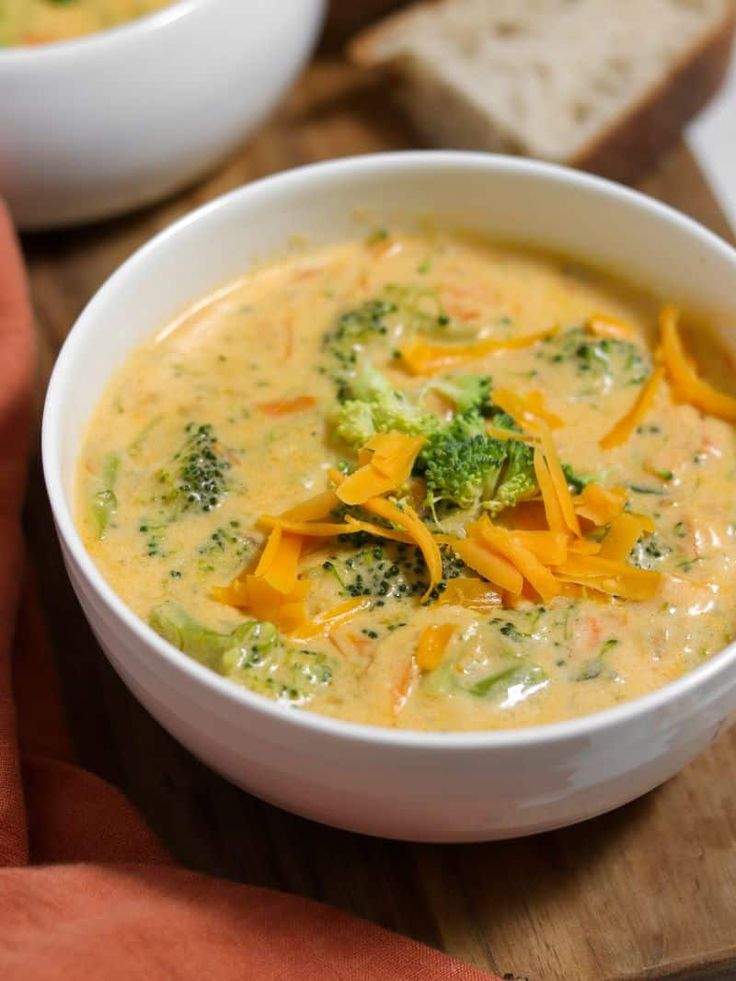 a bowl of broccoli cheese soup on a cutting board with two slices of bread