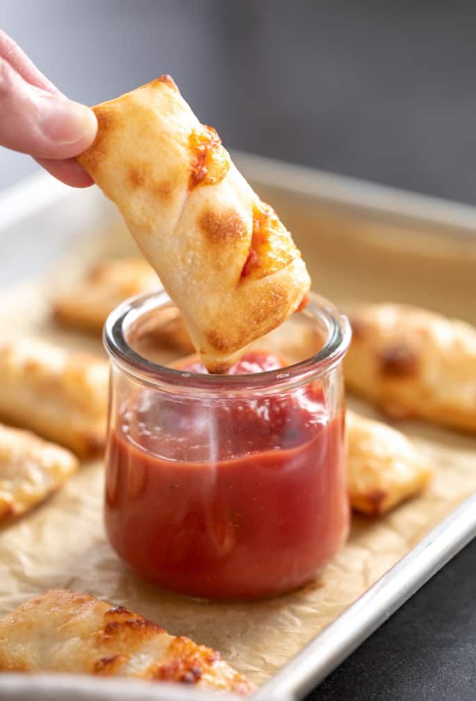 a person dipping some food into a small glass jar filled with ketchup and cheese