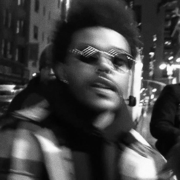 a black and white photo of a woman with glasses on her face in the city at night