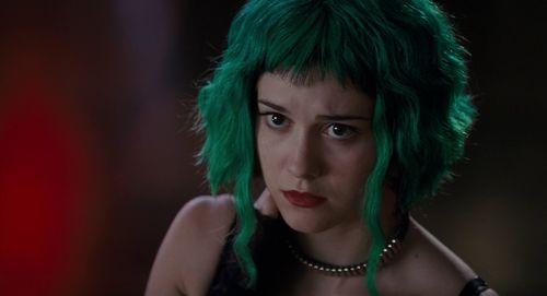 a woman with green hair and piercings on her head looking at the camera in a dark room