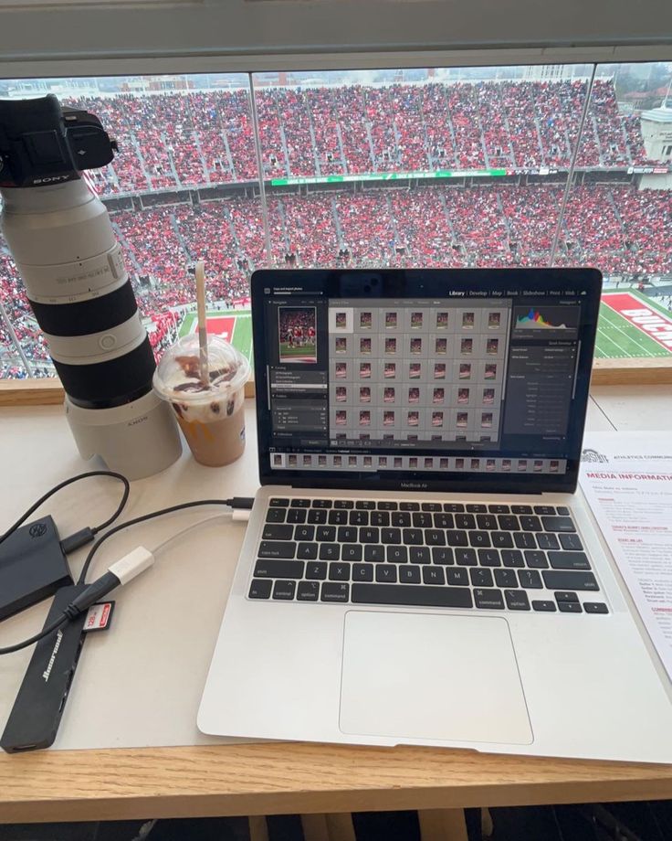 an open laptop computer sitting on top of a wooden desk in front of a large stadium