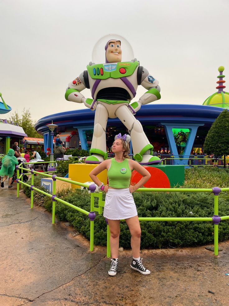 a woman standing in front of a toy story land attraction with buzz lightyear figure