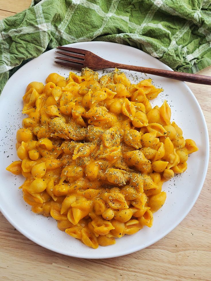 a white plate topped with macaroni and cheese covered in seasoning next to a fork