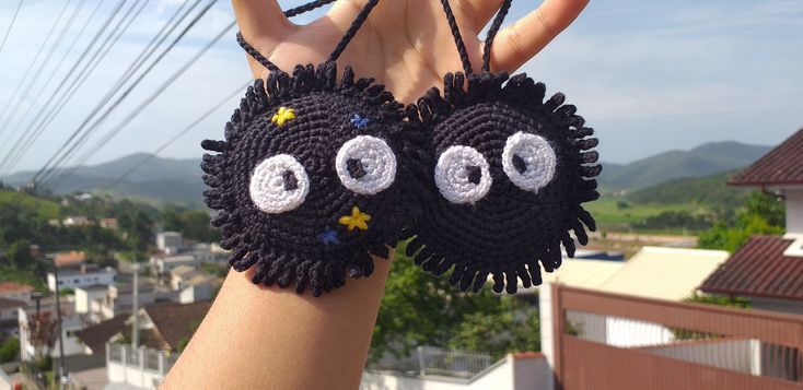 a person holding up two crocheted eyes and stars on their fingers with houses in the background