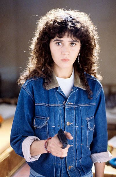 a woman with curly hair is holding a remote control in her hand and looking at the camera