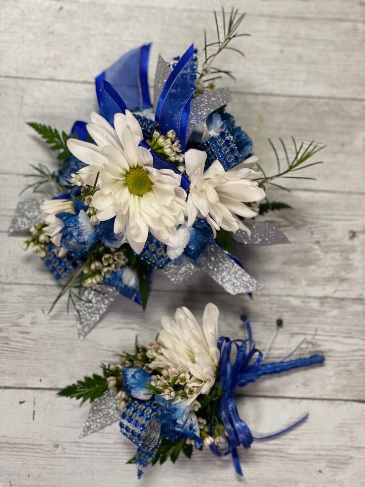 White daisies, tinted royal blue mini carnations with royal blue glitter sprinkled on them.  We used wax flower for fill and royal blue and silver ribbon. Prom Flowers Corsage Royal Blue, Royal Blue Homecoming Flowers, Royal Blue And Silver Corsage, Royal Blue Corsage And Boutonniere Prom, Royal Blue And White Corsage, Blue And Silver Corsage, Royal Blue Corsage And Boutonniere, Blue And White Corsage, Royal Blue Corsage