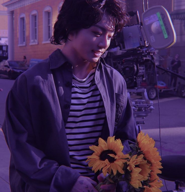 a young man holding a bouquet of sunflowers in front of a movie set