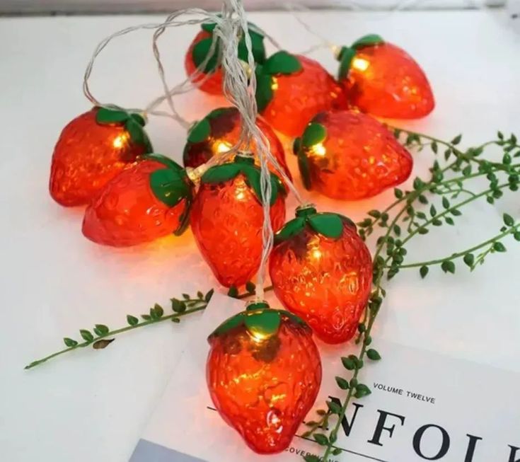 red strawberry shaped string lights with green leaves on white table top next to card and envelope