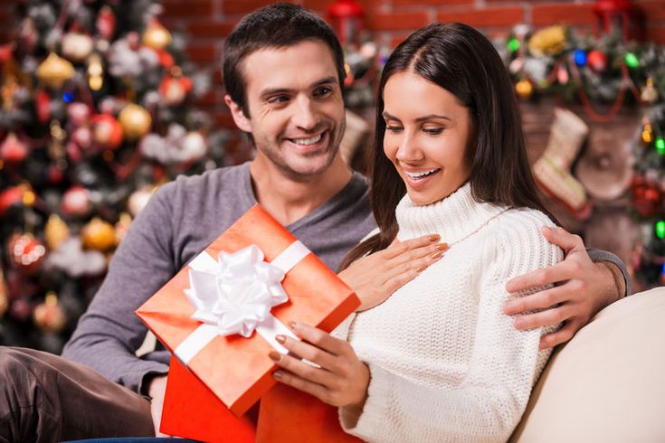 a man and woman sitting on a couch holding a present