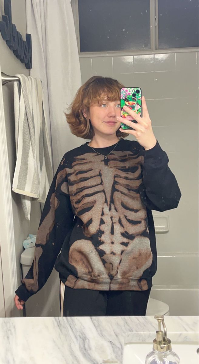 a woman taking a selfie in the bathroom with her skeleton sweater over her shoulders