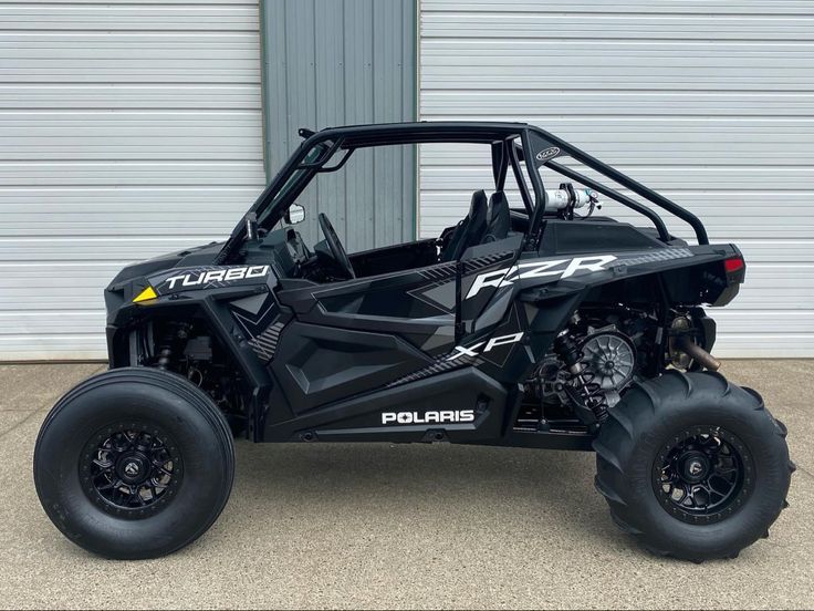 the polaris rzr xp4 is parked in front of a garage door